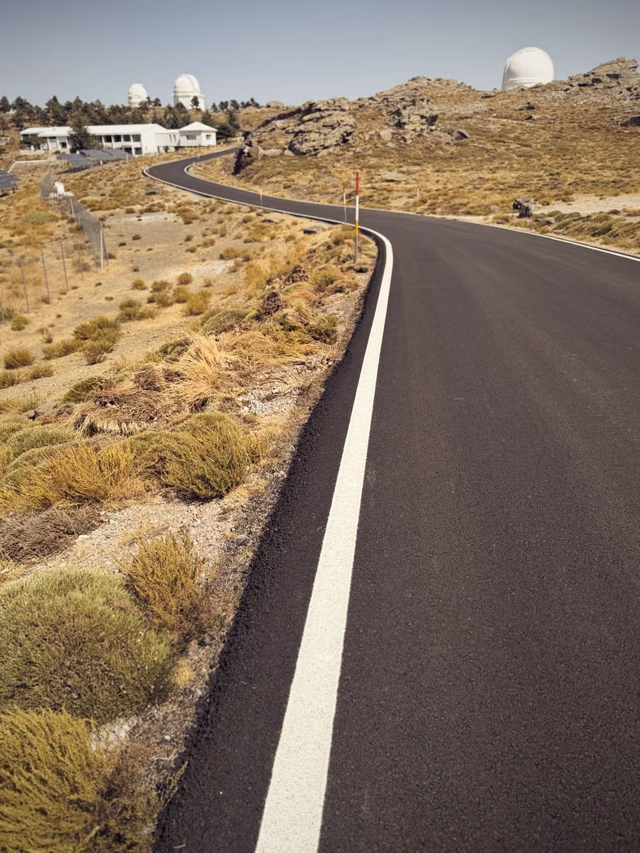 Fresh black tarmac curving past white observatory domes on a dry mountain top.