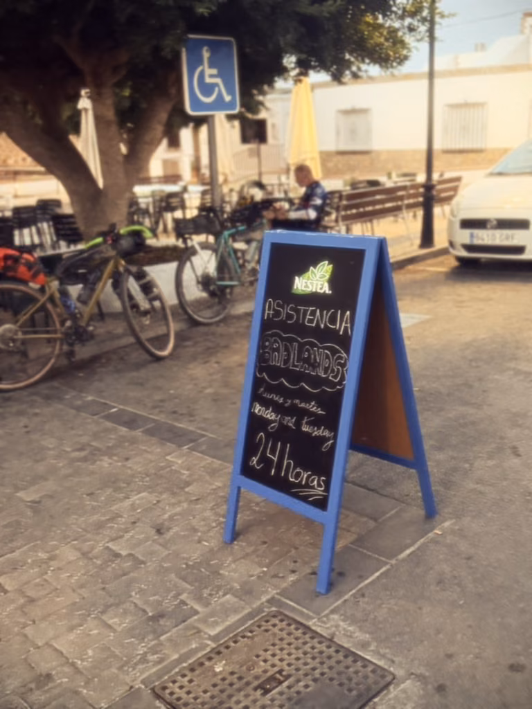 A chalkboard in Enix advertises 24-hour assistance for Badlands. Loaded bikes stand behind it.