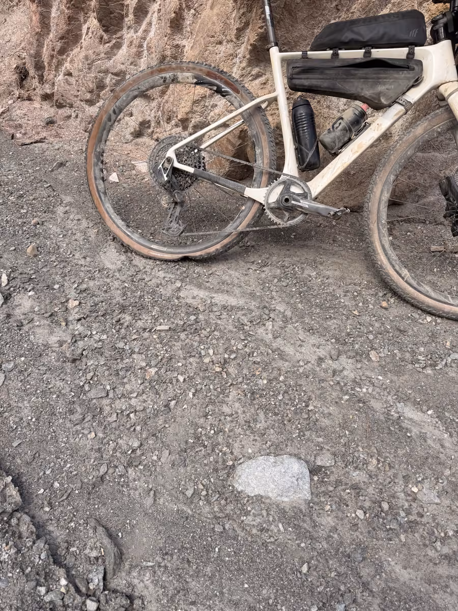 A loaded gravel bike leaning against a red earth bank on a rocky track, rear wheel toward the camera.