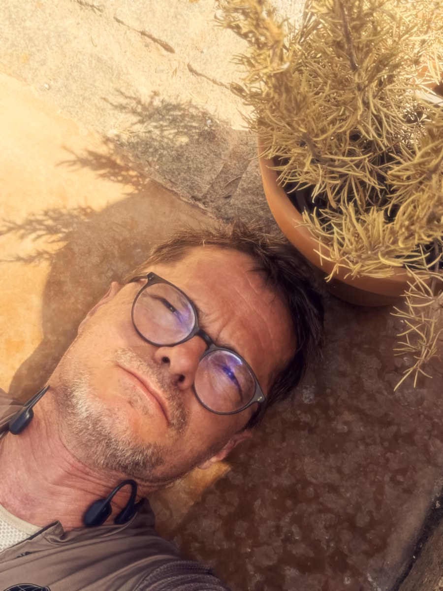 A rider lying on the pavement, glasses on, earbud in, a potted plant beside his head.