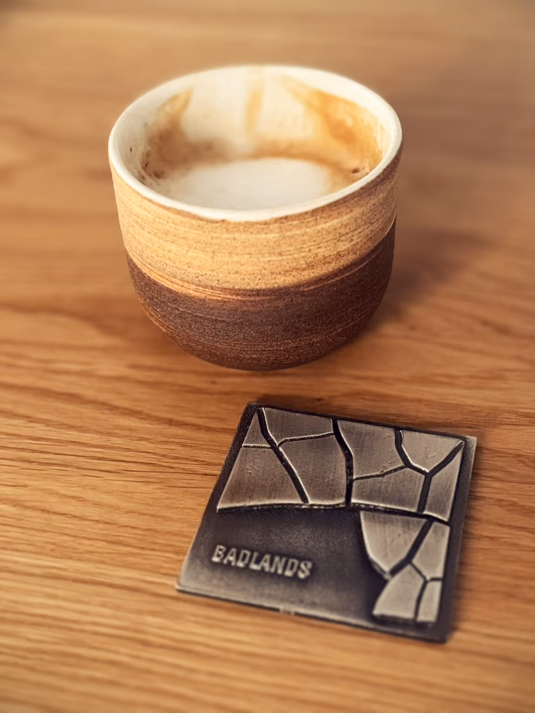 The same medal on a wooden table next to a coffee in a brown pottery cup.