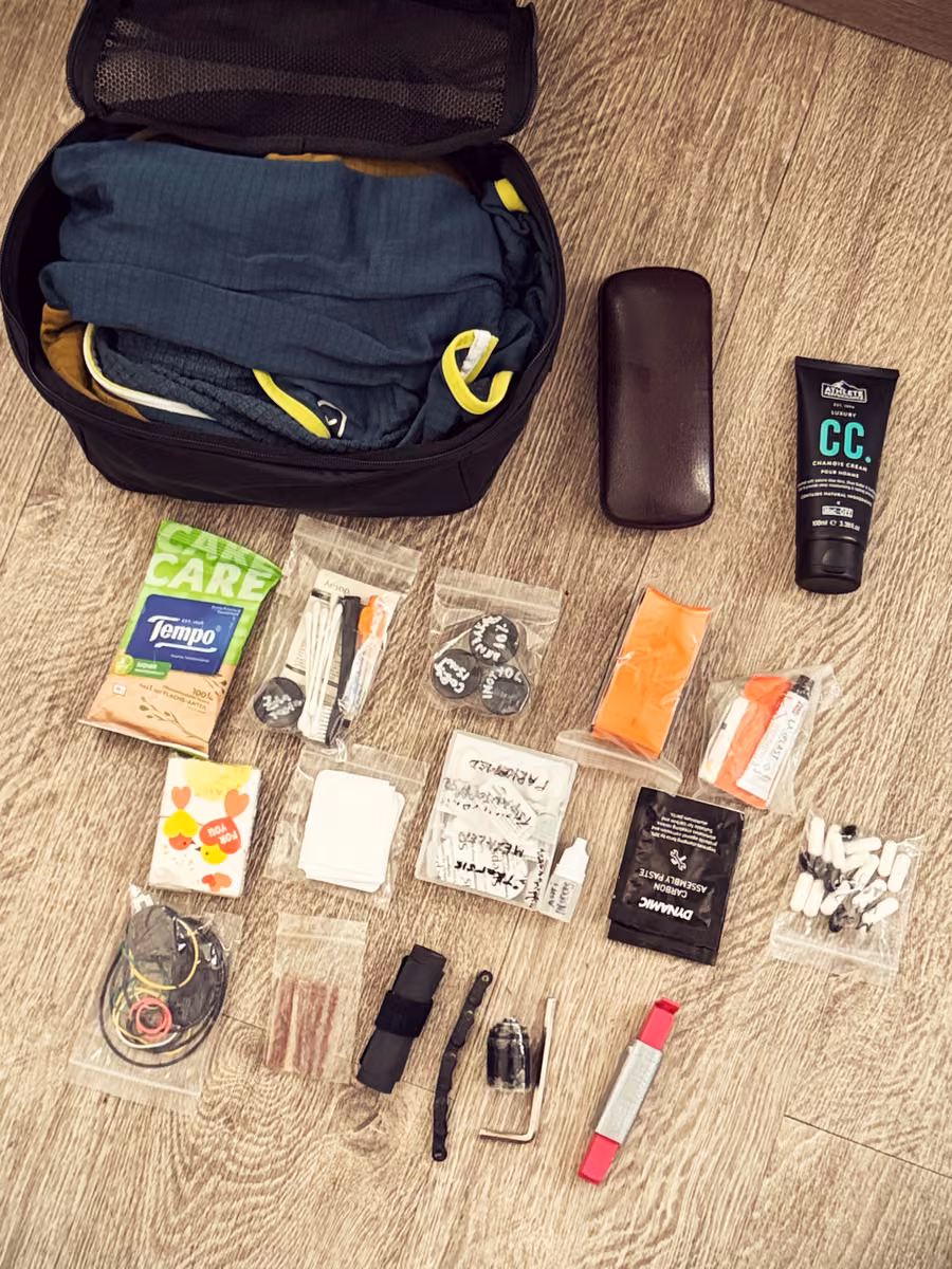 A bag holding folded layers, with tools, spares and toiletries arranged beside it.