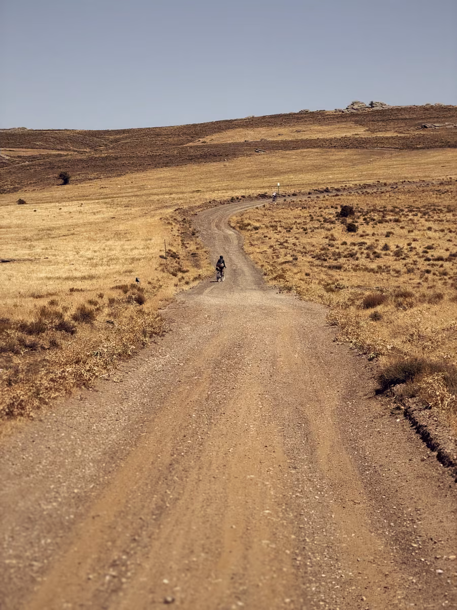 A lone rider on a gravel road winding through dry high plateau grassland.