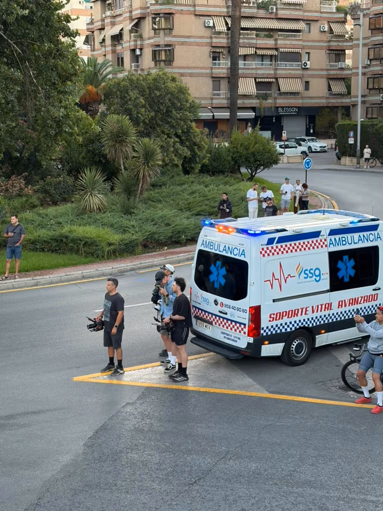 People holding cameras stand beside an ambulance below the steps.