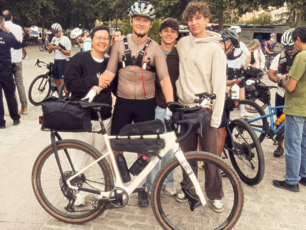 Four people pose behind a loaded cream-colored gravel bike in the start square.
