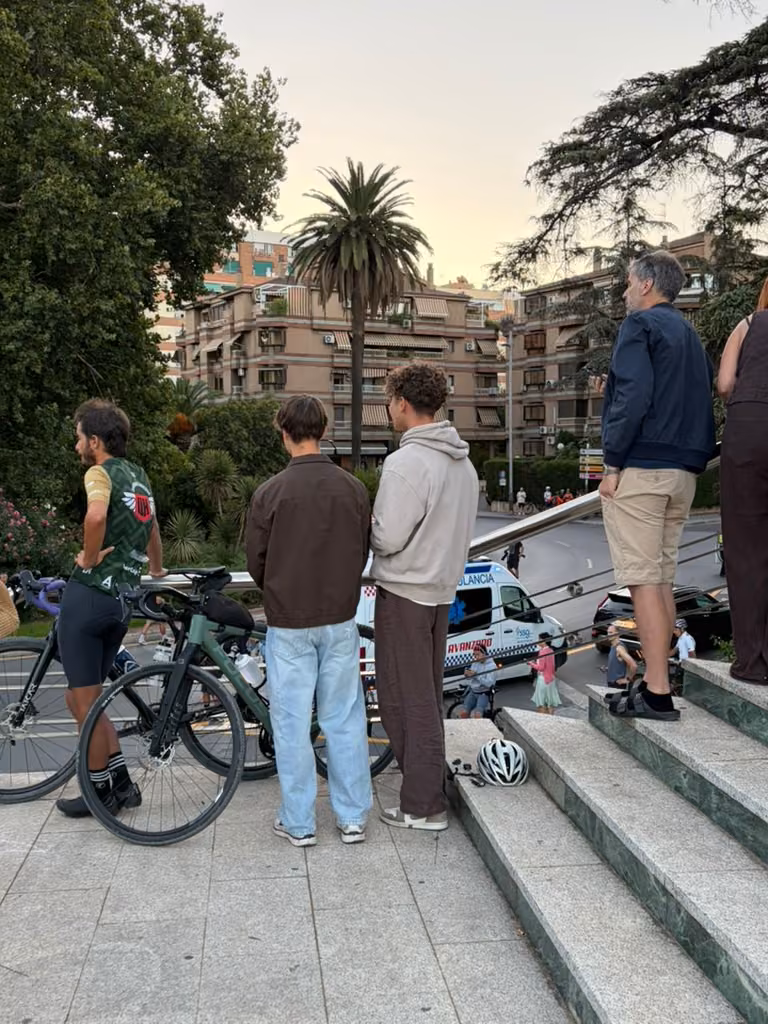 Spectators and a rider stand on the steps overlooking the road beside the square.